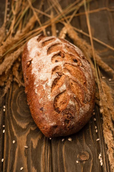 Selective focus of fresh baked bread loaf with spikelets on wooden surface — Stock Photo