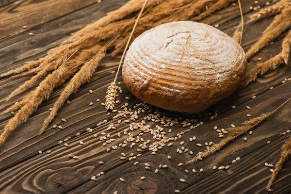 Fresh baked white bread loaf with spikelets on wooden surface — Stock Photo