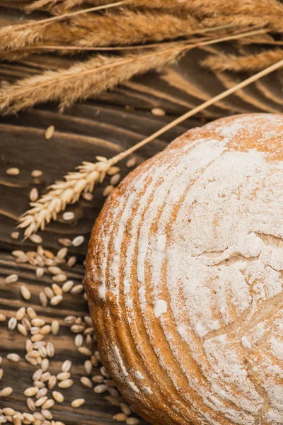 Selective focus of fresh baked bread loaf with spikelets on wooden surface — Stock Photo