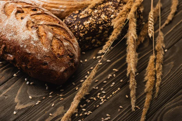 Pagnotte di pane appena sfornate con spighette su superficie di legno — Foto stock