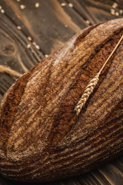 Close up view of fresh baked brown bread loaf with spikelet on wooden surface — Stock Photo