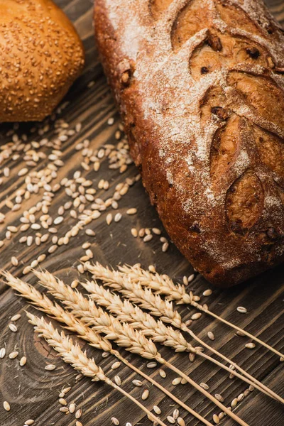 Pagnotte di pane appena sfornate con spighette su superficie di legno — Foto stock