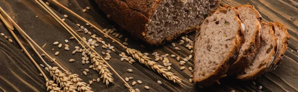 Cut fresh baked bread with spikelets on wooden surface, panoramic shot — Stock Photo