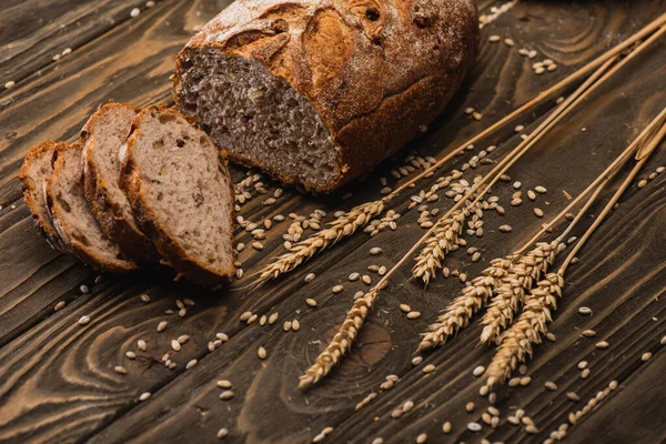 Pain frais coupé au four avec des épillets sur la surface en bois — Photo de stock