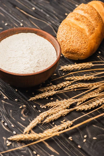 Fresh baked white bread loaf with wheat flour in bowl and spikes on wooden surface — Stock Photo