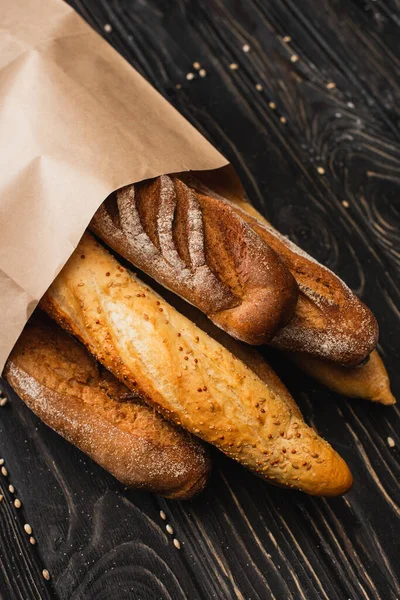 Fresh baked baguette loaves in paper bag on wooden surface — Stock Photo