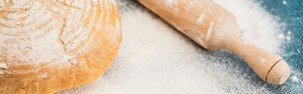 Close up view of fresh baked bread and wooden rolling pin on flour, panoramic shot — Stock Photo