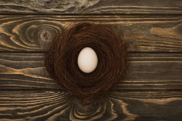Top view of fresh chicken egg in nest on wooden surface — Stock Photo