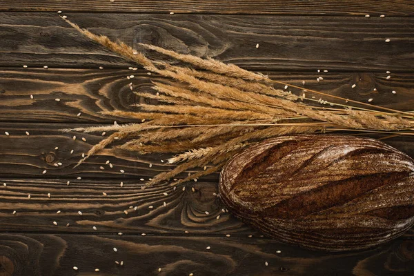 Top view of fresh baked bread loaf with spikelets on wooden surface — Stock Photo