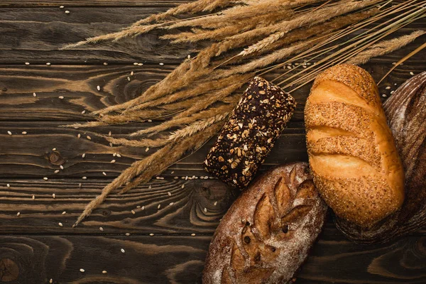 Top view of fresh baked bread loaves with spikelets on wooden surface — Stock Photo