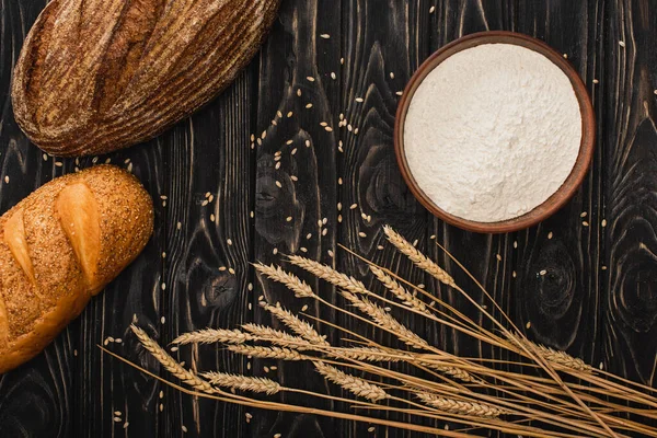 Vista dall'alto di pane appena sfornato ama con spikelets e farina su superficie di legno — Foto stock