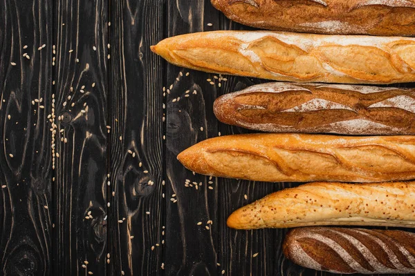 Vue de dessus des pains de baguette fraîchement cuits sur une surface noire en bois — Photo de stock