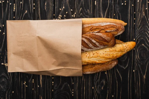 Top view of fresh baked baguette loaves in paper bag on wooden black surface — Stock Photo