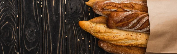 Top view of fresh baked baguette loaves in paper bag on wooden black surface, panoramic shot — Stock Photo