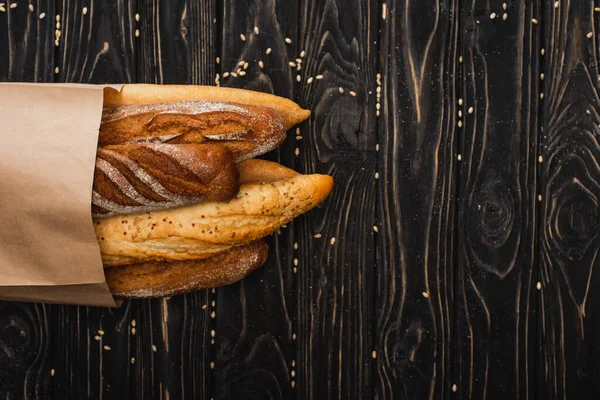 Top view of fresh baked baguette loaves in paper bag on wooden black surface — Stock Photo