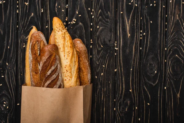 Vue du dessus des pains de baguette frais cuits au four dans un sac en papier sur une surface noire en bois — Photo de stock