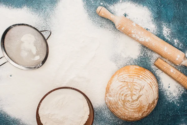 Top view of fresh baked bread loaf near rolling pin and sieve on flour — Stock Photo