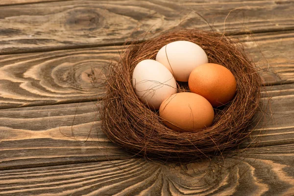 Fresh chicken eggs in nest on wooden surface — Stock Photo