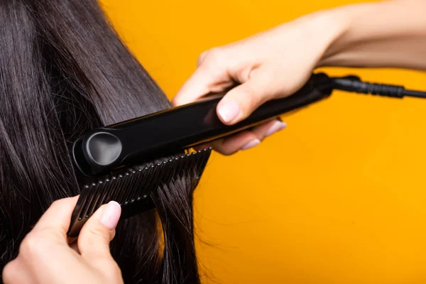 Vista ritagliata del parrucchiere utilizzando piastra per capelli e pettine isolato su giallo — Foto stock