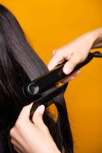 Vista recortada de peluquería usando plancha de pelo y peine aislado en amarillo - foto de stock