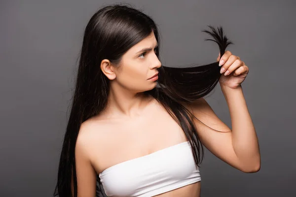 Worried brunette long haired woman looking at split ends isolated on black — Stock Photo