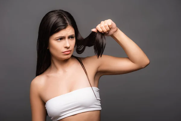 Aufgebracht brünette langhaarige Frau schaut auf Spliss isoliert auf schwarz — Stockfoto