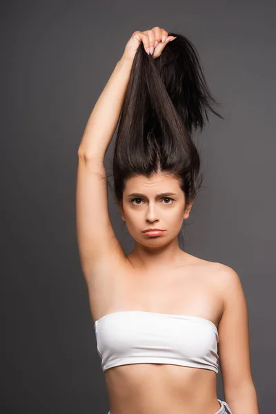 Turbato bruna donna tenendo i capelli danneggiati isolati su nero — Foto stock