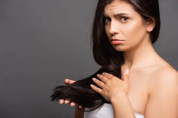 Bouleversé brunette femme toucher cheveux isolés sur noir — Photo de stock