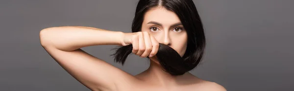 Morena desnuda sosteniendo el pelo cerca de la cara aislado en negro, plano panorámico - foto de stock