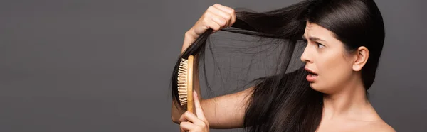 Naked shocked brunette woman brushing hair isolated on black, panoramic shot — Stock Photo