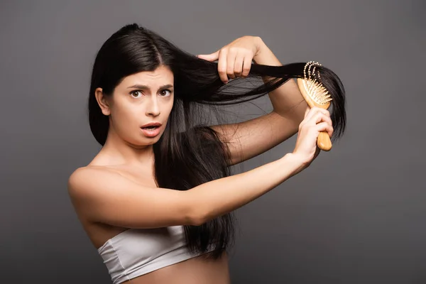 Shocked brunette woman brushing hair isolated on black — Stock Photo