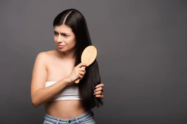 Sad brunette woman brushing hair isolated on black — Stock Photo