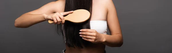 Vista cortada de mulher morena escovando cabelo brilhante isolado em preto, tiro panorâmico — Fotografia de Stock