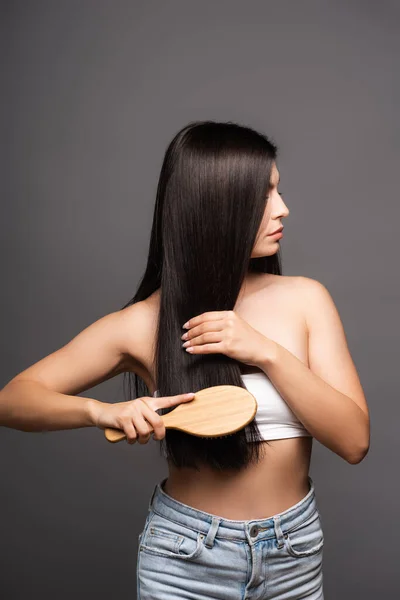 Vista cortada de mulher morena escovando cabelo brilhante isolado no preto — Fotografia de Stock