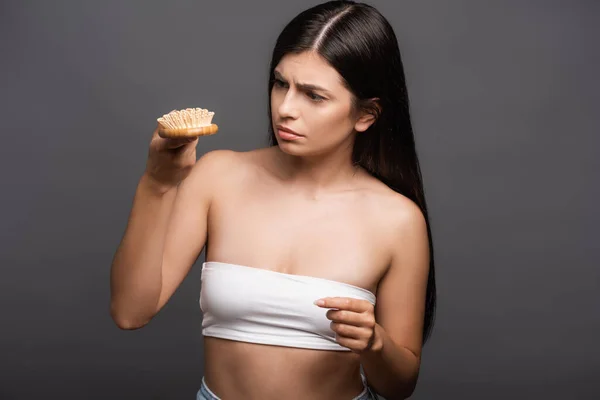 Inquiet brunette femme regardant brosse à cheveux isolé sur noir — Photo de stock