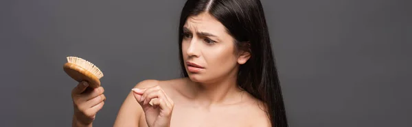 Nudo preoccupato bruna donna guardando spazzola isolata su nero, colpo panoramico — Foto stock