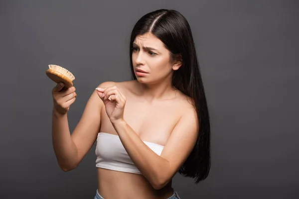 Besorgte brünette Frau schaut auf Haarbürste isoliert auf schwarz — Stockfoto