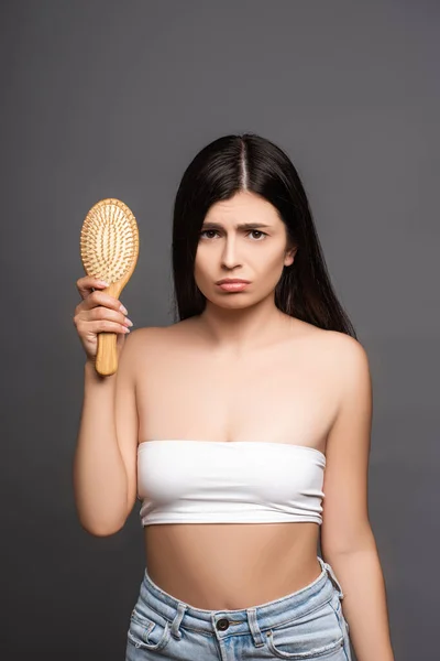 Triste morena segurando escova de cabelo isolado no preto — Fotografia de Stock
