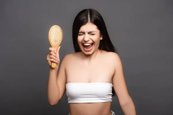 Morena mujer sosteniendo cepillo de pelo y gritando aislado en negro - foto de stock