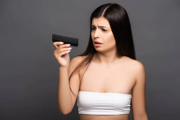 Sad brunette woman looking at comb isolated on black — Stock Photo