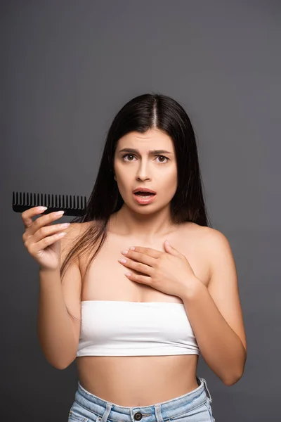 Shocked brunette woman holding comb isolated on black — Stock Photo