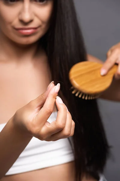 Вибірковий фокус брюнетки жінка тримає втрачене волосся під час чищення ізольовано на чорному — стокове фото