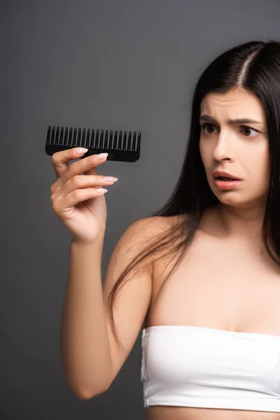 Shocked brunette woman looking at comb isolated on black — Stock Photo