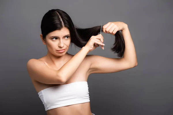 Worried brunette woman cutting hair isolated on black — Stock Photo