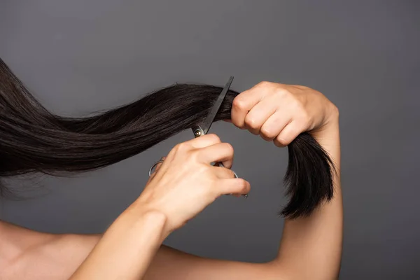 Cropped view of naked brunette woman cutting hair isolated on black — Stock Photo