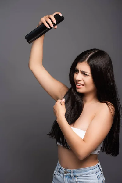 Morena de cabelos longos mulher aplicando spray de cabelo com olhos fechados isolados em preto — Fotografia de Stock