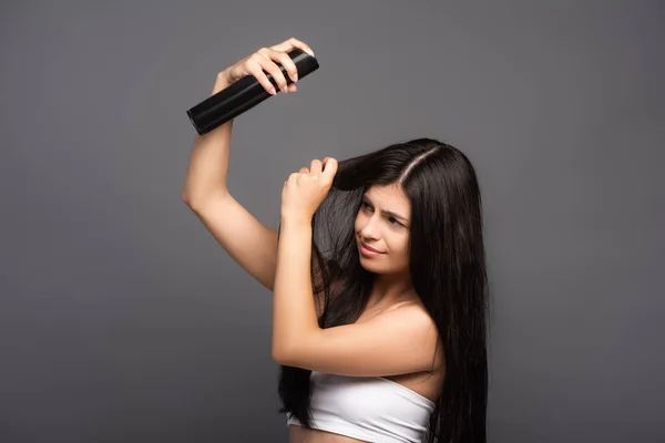 Брюнетка длинноволосая женщина применяет лак для волос изолированный на черном — стоковое фото
