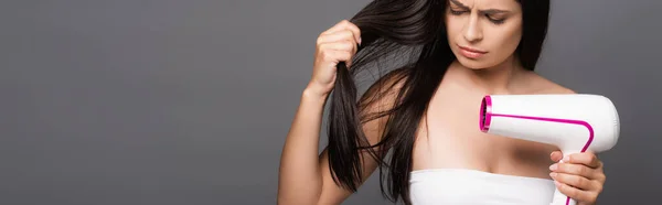 Preoccupato bruna dai capelli lunghi donna utilizzando asciugacapelli isolato su nero, colpo panoramico — Foto stock