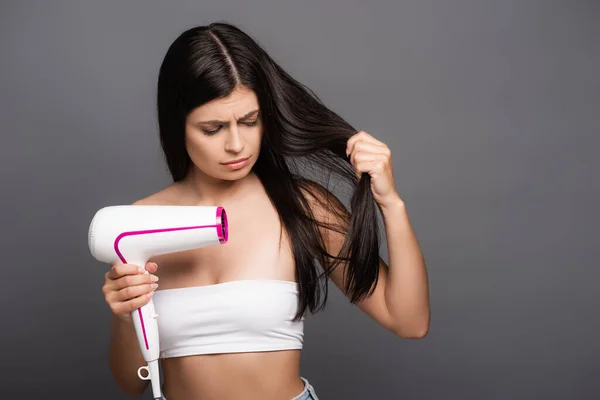 Morena preocupada mujer de pelo largo utilizando secador de pelo aislado en negro - foto de stock