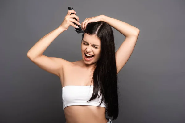 Morena mujer de pelo largo afeitado cabeza con afeitadora eléctrica y gritando aislado en negro - foto de stock